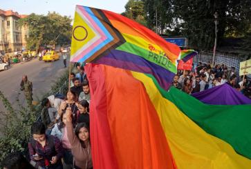 Pride parade through a street with a massive rainbow flag